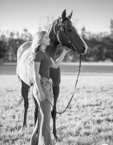 a woman standing next to a horse in a field