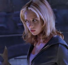 a woman with blonde hair wearing a black leather jacket and looking at something in her hand