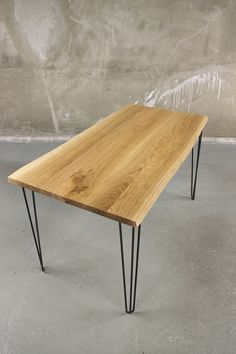 a wooden table with black hairpinks on it and a concrete wall in the background