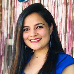 a woman with long dark hair and blue dress smiling at the camera in front of a bamboo wall