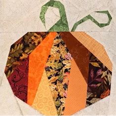 a patchwork pumpkin quilted on top of a white piece of cloth with green ribbon