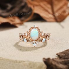 an opal and diamond ring sitting on top of a table next to some leaves