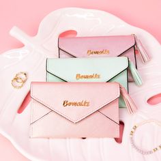 three pink and green envelopes sitting on top of a white plate with gold lettering