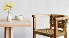 a wooden table with a white vase and yellow flowers on it next to a chair