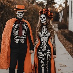 two people dressed up in skeleton costumes walking down a sidewalk with pumpkins on their heads