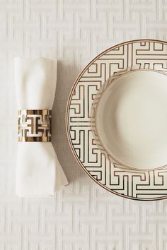 a white plate with gold trim next to a napkin on top of a white tablecloth