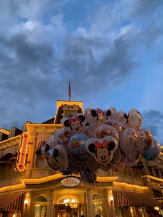 mickey mouse balloons in front of a building at night with the sky lit up behind them