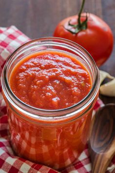 a glass jar filled with tomato sauce on top of a red checkered cloth next to two tomatoes