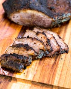 some meat is sitting on a cutting board next to another piece of meat that has been cut in half