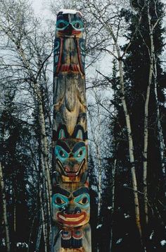 a totem pole in front of some trees with snow on the ground around it