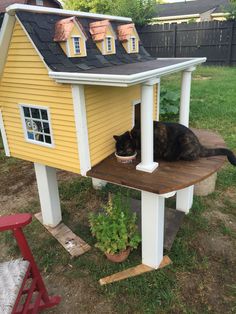 a black cat sitting on top of a wooden table next to a yellow and white house