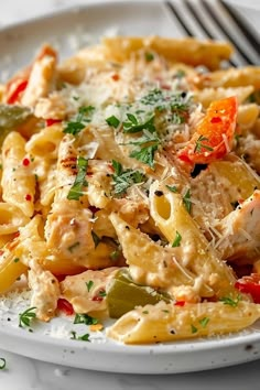 a white plate topped with pasta covered in chicken and vegetables next to a silver fork