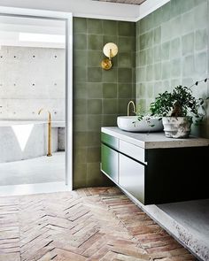 a bathroom with two sinks and green tiles on the walls, along with a gold faucet