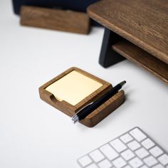 a desk with a pen, notepad and wooden box on it next to a keyboard