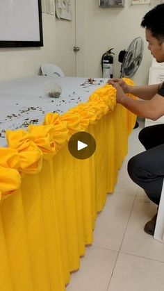 a man kneeling down next to a table covered in yellow cloths