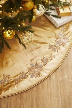 a christmas tree skirt with gold trimmings and ornaments on the floor next to it