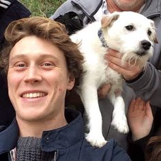 a man holding a white dog in front of two other people and smiling at the camera