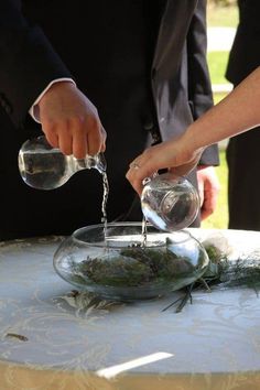 two people pouring water into a bowl on top of a white cloth covered tablecloth