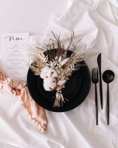 a table setting with black plates, forks and napkins on top of white linen