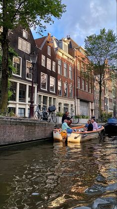 some people are in small boats on the water near buildings and bicycles parked along the side of the street