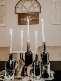 candles are lit in black bottles with writing on the wall behind them that says gather