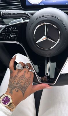 a woman is holding the steering wheel of a mercedes car with tattoos on her arm