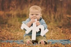 a baby sitting on the ground holding a large white letter with an x in it's mouth