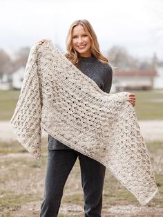 a woman is holding up a crocheted shawl