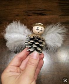 a hand holding a small pine cone angel ornament on top of a wooden table