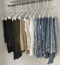 several pairs of jean jackets hanging on a white rail and some hangers in front of them