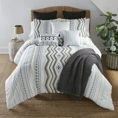 a bed with white and black comforters in a room next to a potted plant