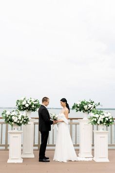 a bride and groom standing next to each other in front of some white flower arrangements