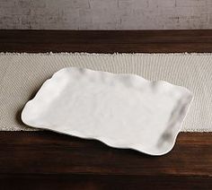 an empty white plate sitting on top of a wooden table next to a striped place mat