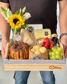 a man holding a wooden box filled with different types of food and wine, along with flowers