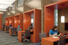 two people working on their laptops in an open area with orange walls and chairs