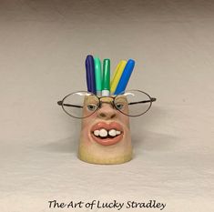 a ceramic head with glasses and pencils sticking out of it's forehead that says the art of lucky stanley