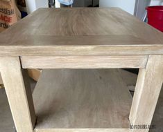 a wooden table sitting on top of a floor next to a red trash can in a room