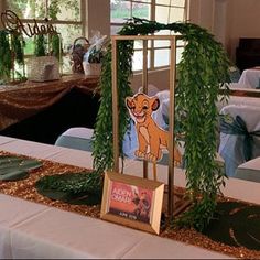 the table is set up for an event with pictures and greenery on it's sides