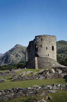 an old stone tower sitting on top of a lush green field next to mountains in the distance