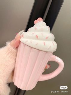 a hand holding a pink cup with white frosting and sprinkles on it