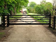 an open gate leading to a dirt road with trees on both sides and a house in the distance