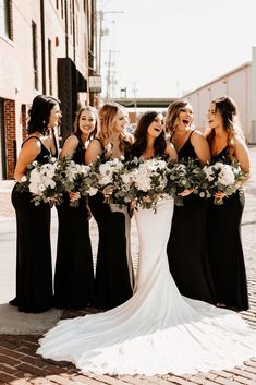 a group of women standing next to each other in front of a brick building holding bouquets