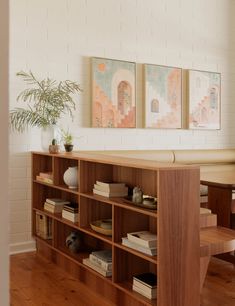 the bookshelf in the living room is made out of wood and has two paintings on the wall