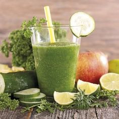 a green smoothie in a glass surrounded by fruits and vegetables