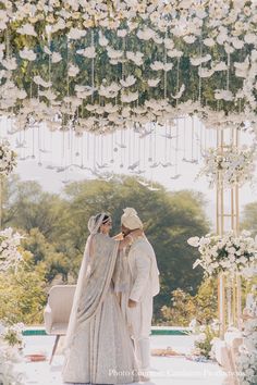 the bride and groom are standing under an arch with white flowers