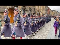 a group of men in uniform marching down the street with people walking by onlookers