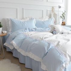 a bed with blue sheets and white ruffles on the bottom, along with a teddy bear