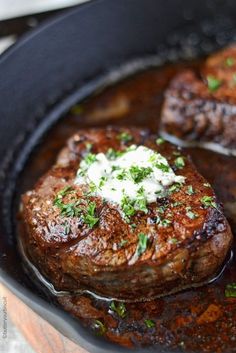 two steaks are cooking in a skillet with sauce and sour cream on top