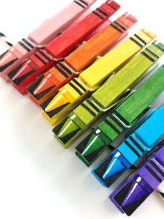 colorful crayons are lined up in a row on a white surface with black handles