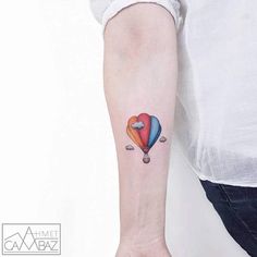 a person with a tattoo on their arm holding a hot air balloon in the shape of a heart